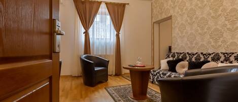 A living room with a wooden door, a black leather chair, a round coffee table with a red object, a patterned sofa, and a patterned wall.