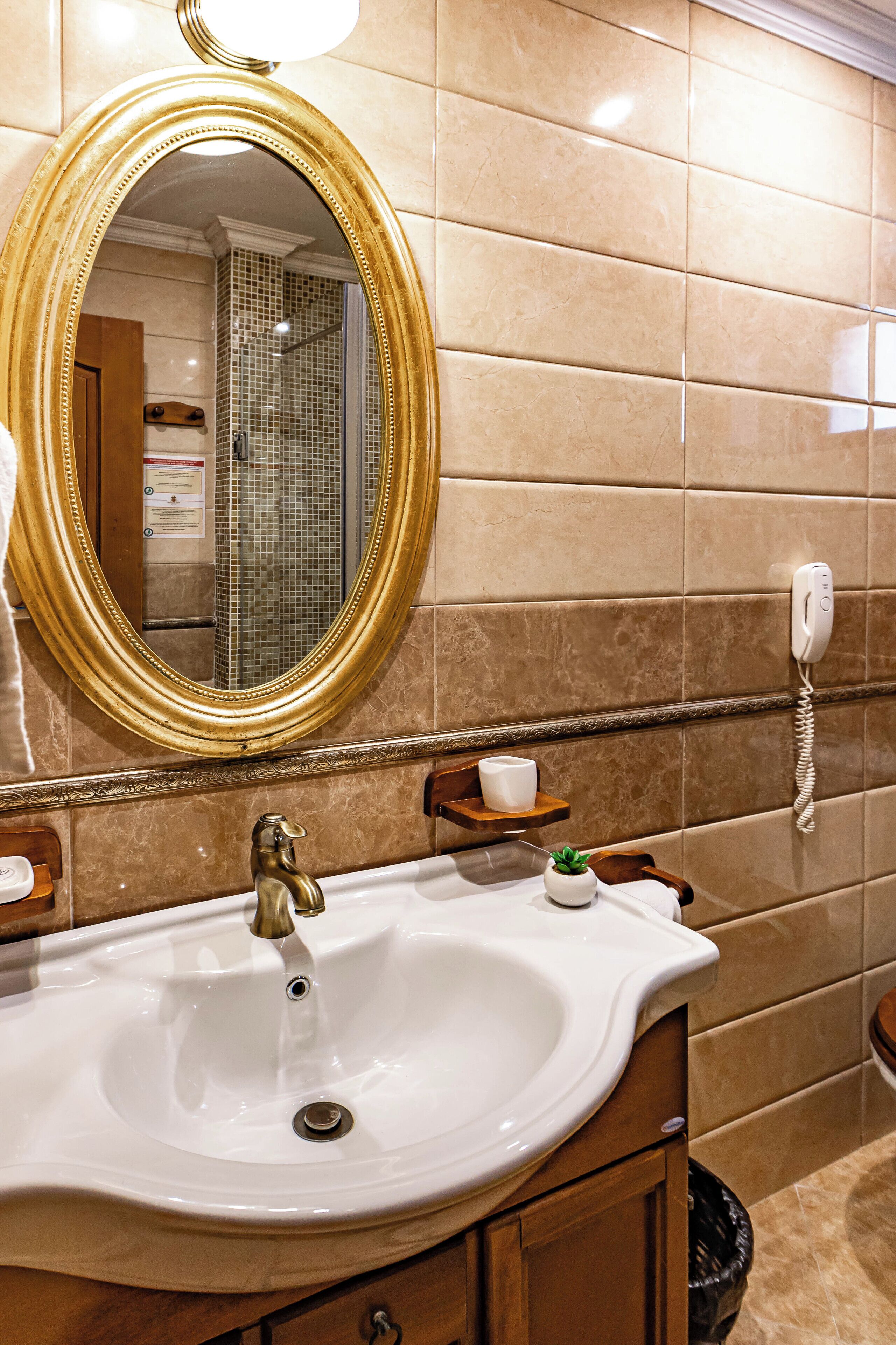 Ein Badezimmer mit einem weißen Waschbecken, einem spiegel mit goldener Rahmung und einem Telefon an der Wand.