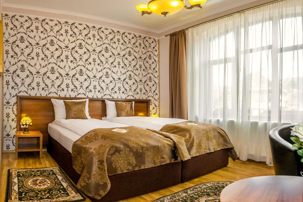 Habitación de hotel con una cama grande, una mesita de noche con lámpara, zona de ducha y vistas a la ciudad a través de la ventana.