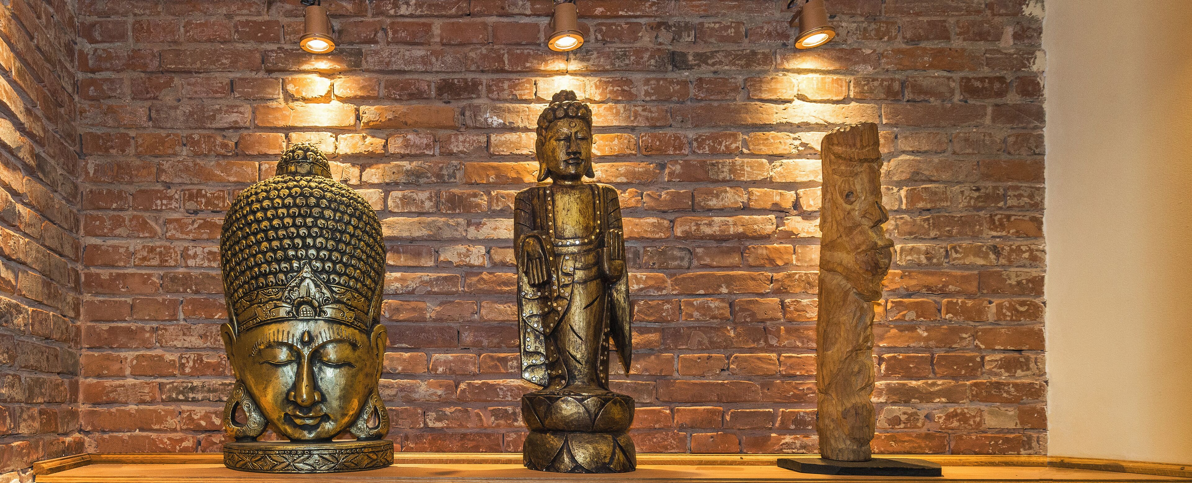 Three statues against a brick wall with lighting above them.
