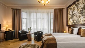 A hotel room with a large bed, two armchairs, a desk with a lamp, and a large window with curtains. - Hotel Boutique Bulevard (Sighisoara)