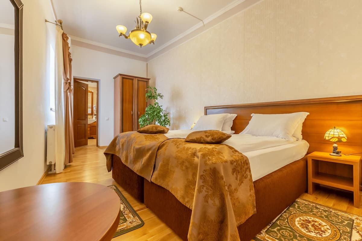 Un dormitorio con una cama grande, cabecera de madera, lámpara de noche y vistas a un pasillo con una planta.