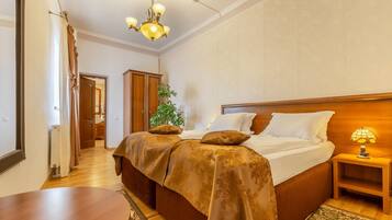 A bedroom with a large bed, wooden headboard, bedside lamp, and a view of a hallway with a plant.