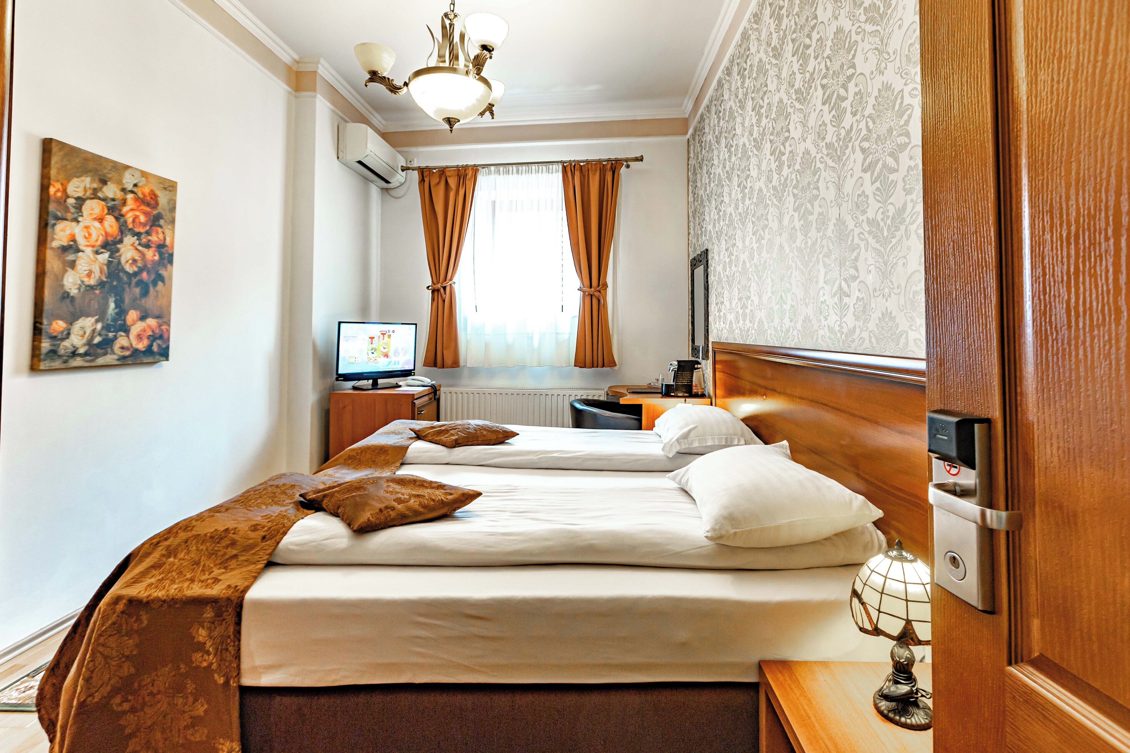 A hotel room with two beds, a desk, a lamp, and a painting on the wall.
