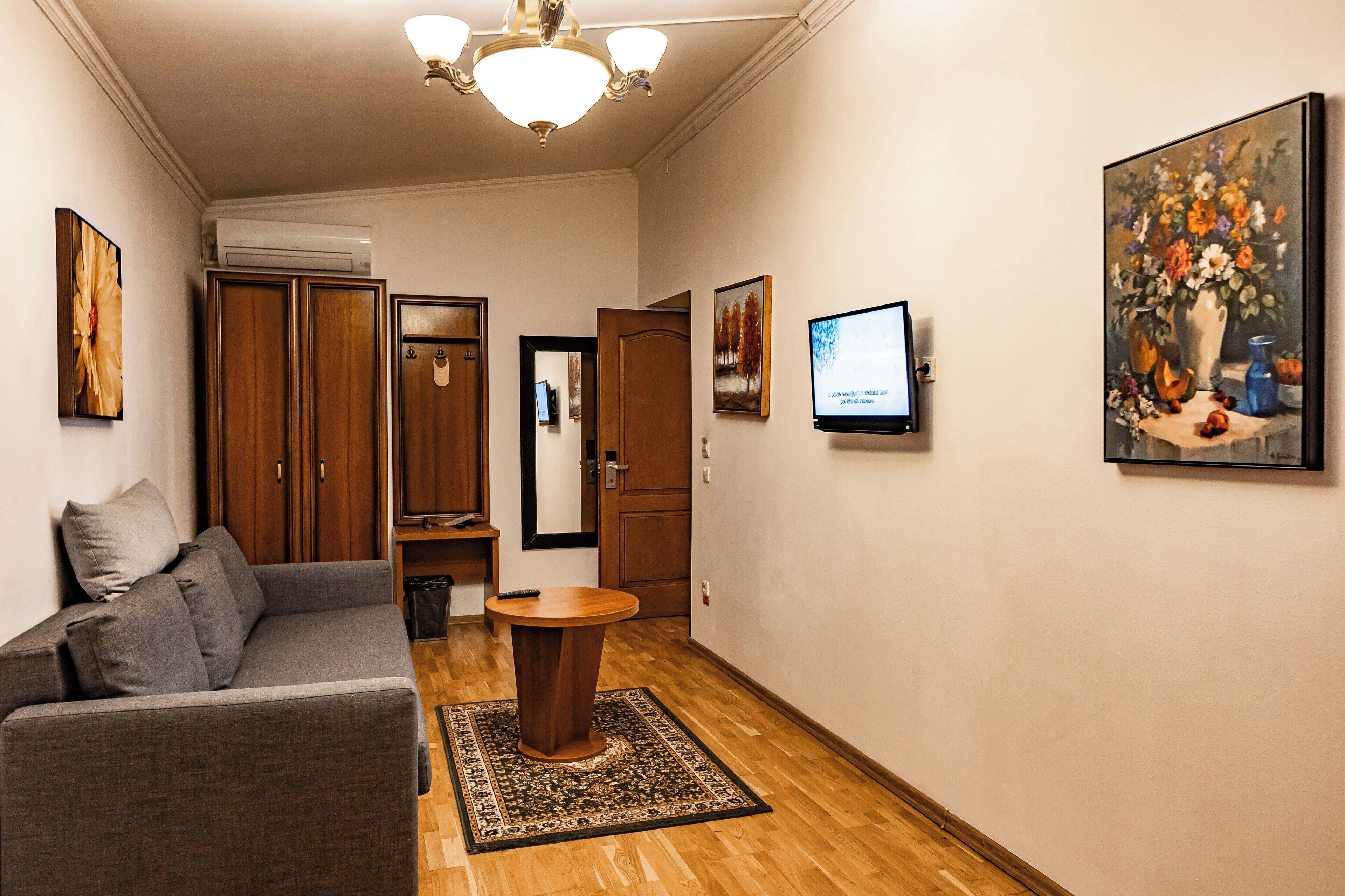 A modern hotel room with a grey sofa, a wooden table, and a painting on the wall.