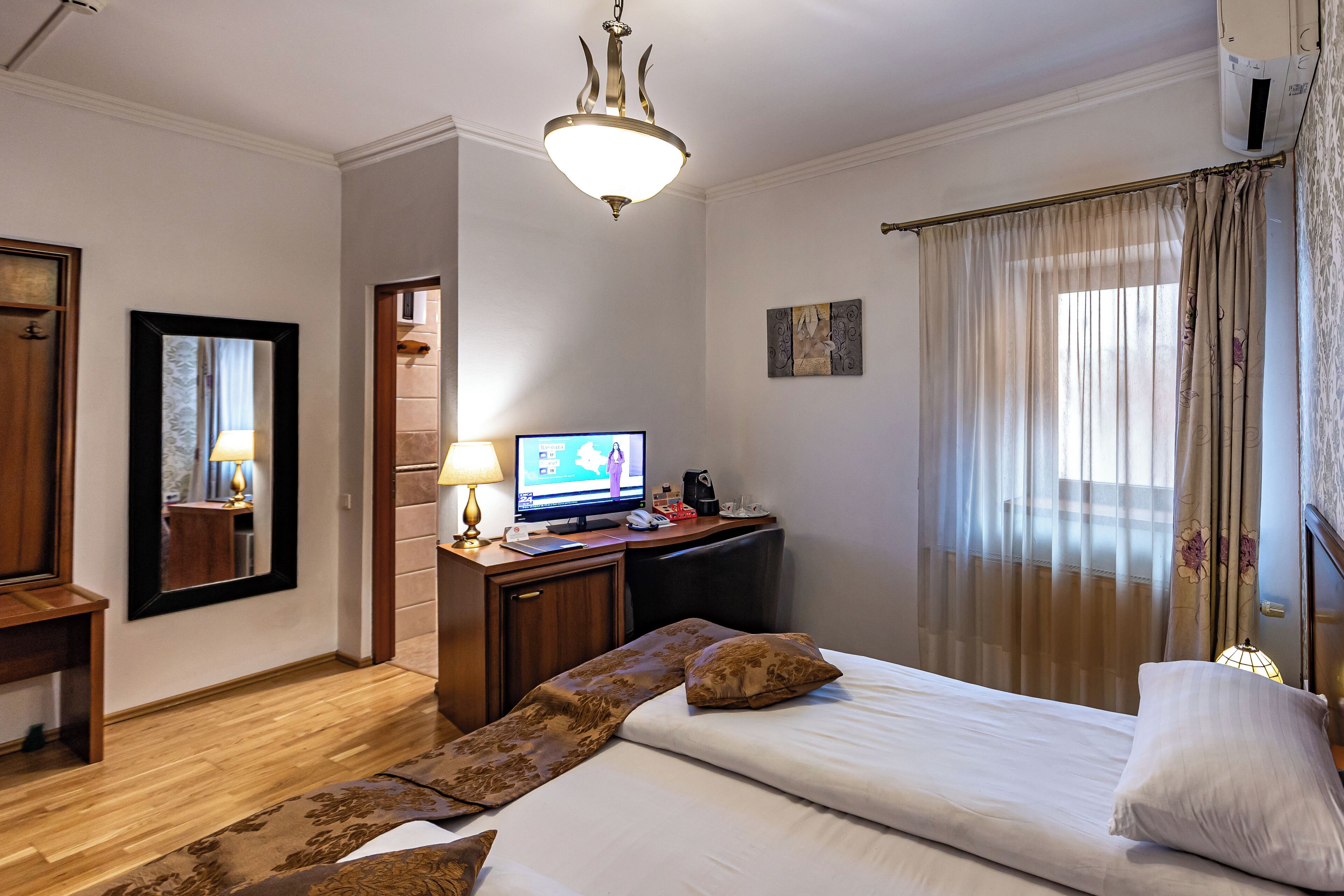 Una camera d'albergo con un letto, una scrivania con un computer, una televisione e una finestra con tende.