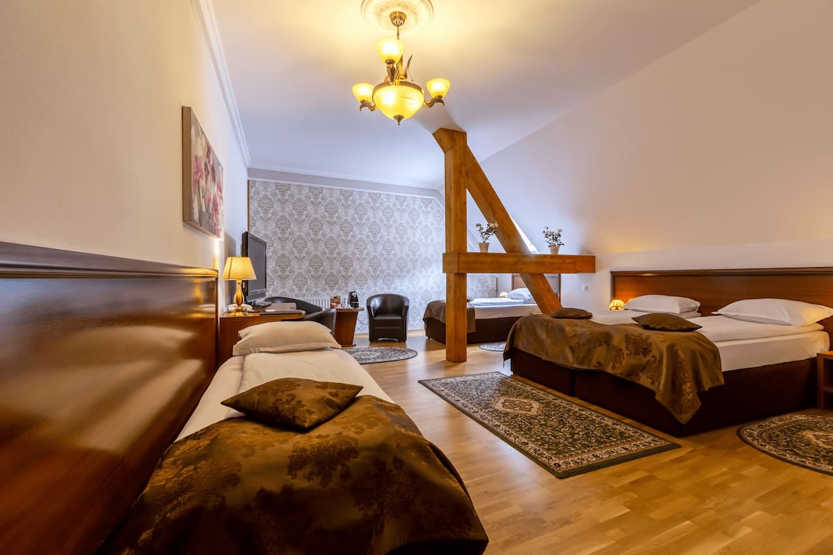 Habitación de hotel con dos camas, una estructura de madera en forma de A, una araña y un papel tapiz estampado.