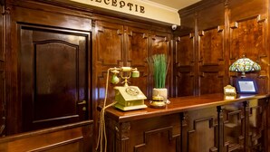 A reception area with a wooden reception desk, a vintage telephone, a vase with green plants, and a decorative lamp. - Hotel Boutique Bulevard (Sighisoara)