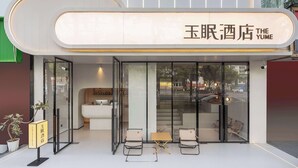 A hotel exterior with a modern design, featuring a large illuminated sign, glass doors, and a seating area outside. - The Yume Hotel (Nanjing)
