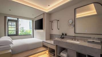 A modern hotel room with a bed, a large mirror, a vanity with a sink, and a television mounted on the wall.