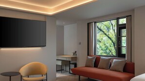 A modern room with a sofa, a chair, a TV, and a window with a view of trees. - The Yume Hotel (Nanjing)