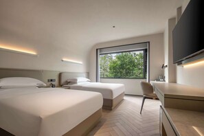 Habitación de hotel moderna con dos camas, un escritorio y un amplio ventanal con vistas a zonas verdes.