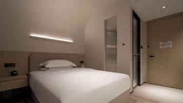 A modern hotel room with a neatly made bed, a bedside table with a clock, and a door with a sign.