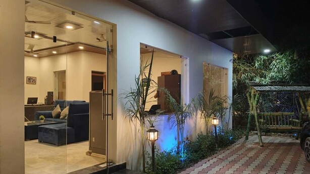 A modern exterior with a glass door entrance, a paved pathway, and outdoor lighting. - Evencia Resort (Ramnagar)