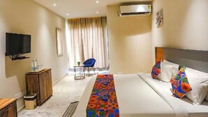 A hotel room with a bed, a TV, a desk, a chair, and an air conditioning unit. - Evencia Resort (Ramnagar)