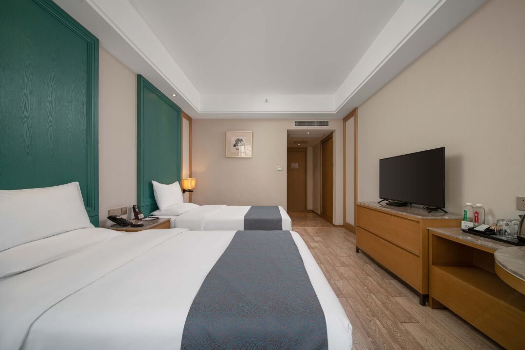 Habitación de hotel con dos camas, televisión, escritorio y lámpara.
