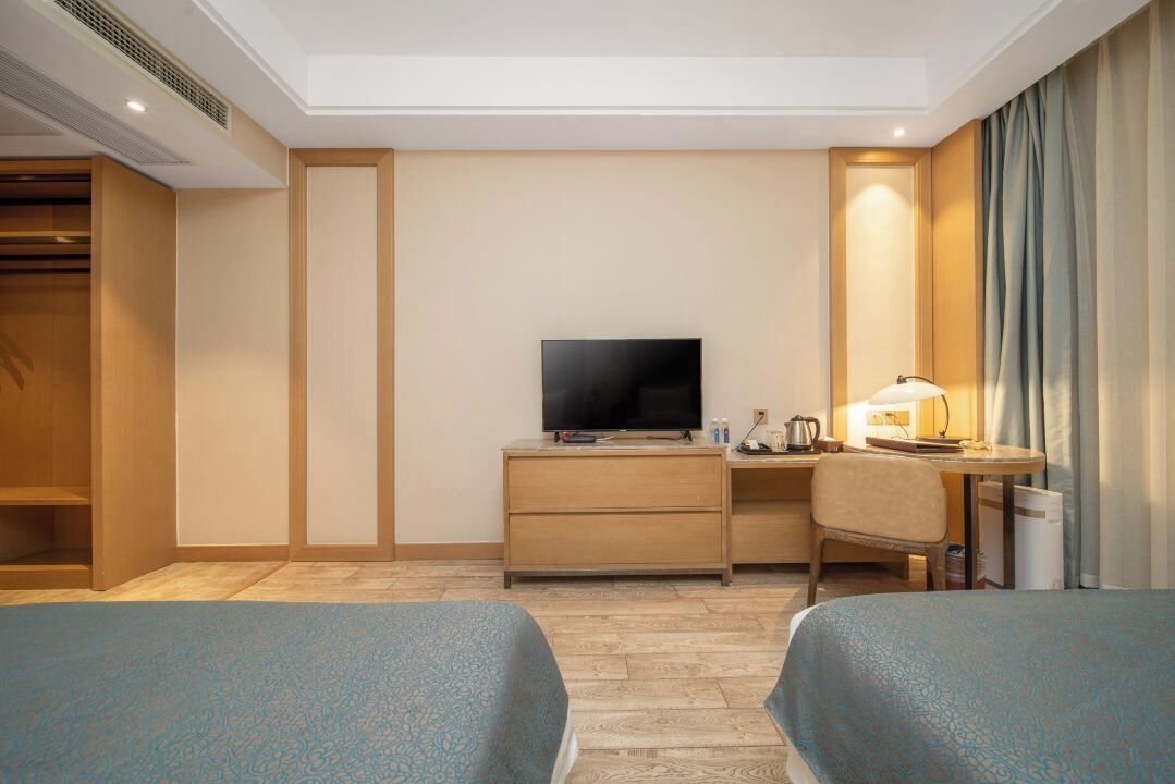 A hotel room with two beds, a desk with a TV, a chair, and a wardrobe.