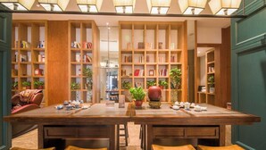 A library-style seating area with wooden tables and benches, surrounded by tall bookshelves filled with books and plants. - World Hotel Hexie Plaza branch (Jinan)