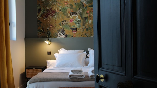 A hotel room with a bed, a bench, a wall-mounted light, and a door. - Town house 14 people - La Rochelle hypercentre Maison Caju Gîte urbain (La Rochelle)