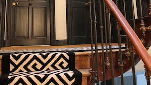 A staircase with a wooden handrail and black balusters, leading to a set of dark wooden doors. - Town house 14 people - La Rochelle hypercentre Maison Caju Gîte urbain (La Rochelle)
