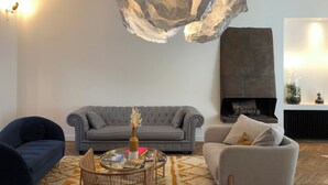 A living room with a grey sofa, a round coffee table with books and a vase, a blue armchair, and a modern chandelier. - Town house 14 people - La Rochelle hypercentre Maison Caju Gîte urbain (La Rochelle)