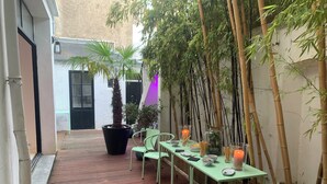An outdoor patio with a table set for dining, surrounded by bamboo plants and chairs. - Town house 14 people - La Rochelle hypercentre Maison Caju Gîte urbain (La Rochelle)