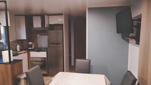 Une cuisine compacte équipée d’un réfrigérateur, d’une cuisinière et d’un évier. Un coin repas avec une table et des chaises est également disponible.