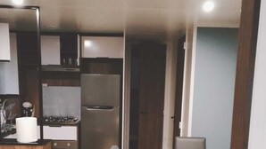 Une cuisine compacte équipée d’un réfrigérateur, d’une cuisinière et d’un évier. On y trouve une table à manger avec des chaises et une poubelle.