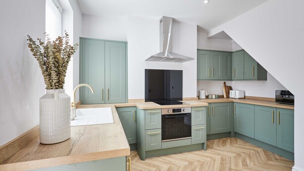 A modern kitchen with teal cabinets, a central island, and a herringbone wood floor. - Host Stay Mayfield (Harrogate)
