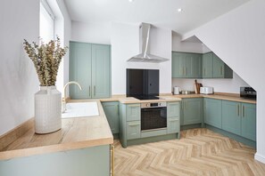 A modern kitchen with teal cabinets, a central island, and a herringbone wood floor. - Host Stay Mayfield (Harrogate)