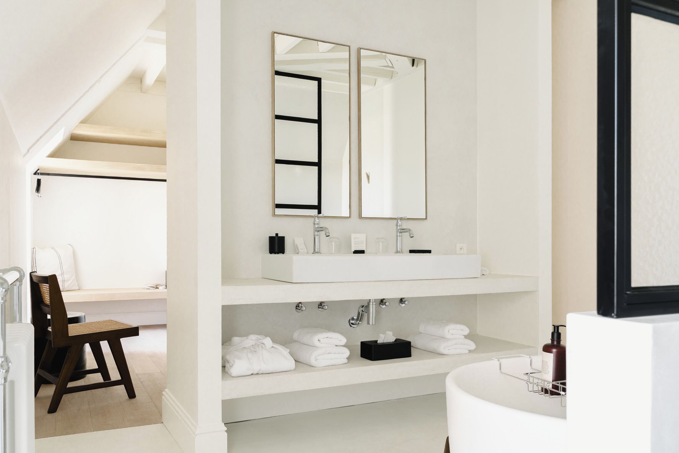 Un baño moderno con lavamanos doble, dos espejos, un banco y un perchero para toallas.
