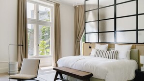 A bedroom with a large bed, a bench, a bedside table, and a floor lamp. - Les Hauts de Sancerre   (Sancerre)