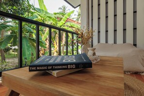 A book titled "The Magic of Thinking Big" on a wooden table with a view of lush greenery and a balcony railing.