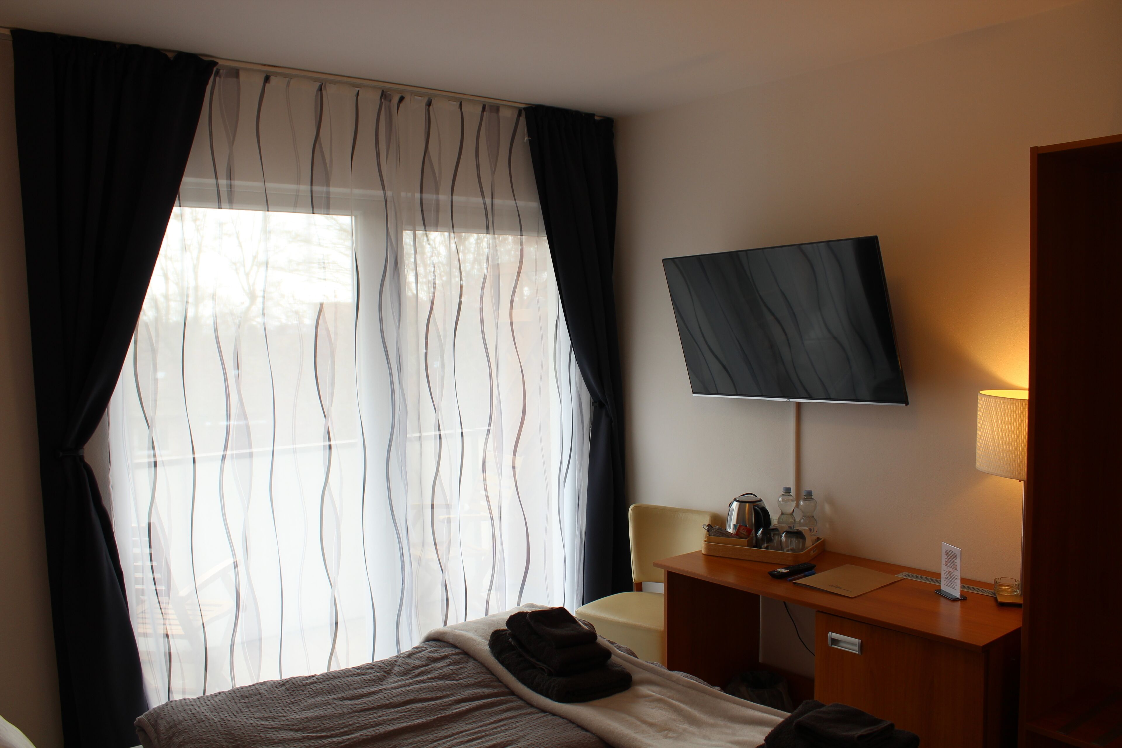 Hotelkamer met een bed, een bureau met een flatscreen-televisie, een lamp en een raam met dunne gordijnen.