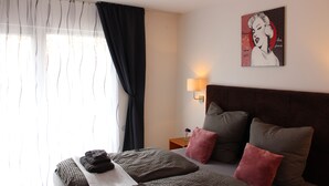 A hotel room with a bed, pillows, a nightstand, a lamp, and a window with curtains. - Burghotel - das Original (Nuremberg)