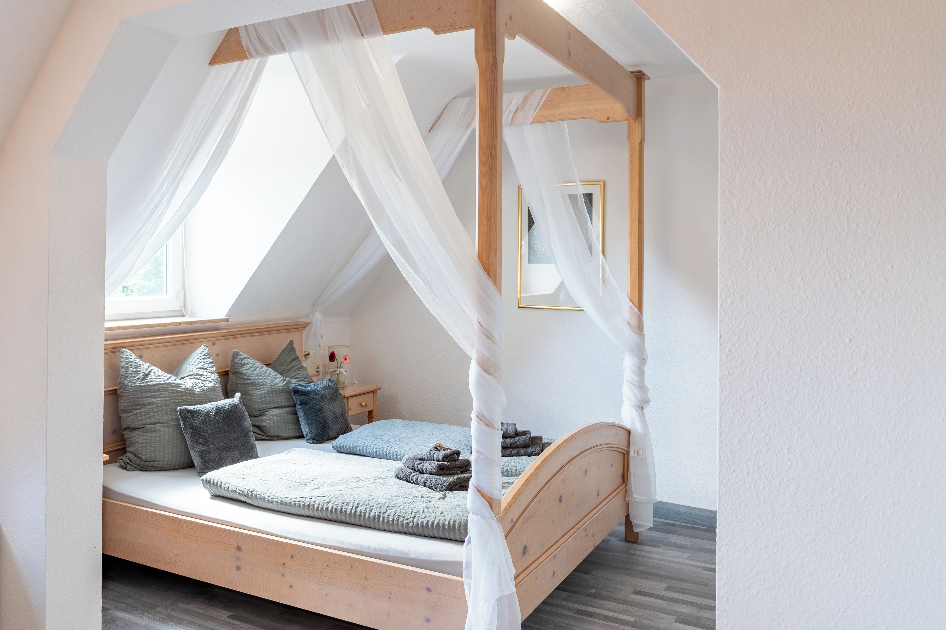 Un dormitorio con una cama de madera con dosel, una mesita de noche y un ventanal con cortinas translúcidas.