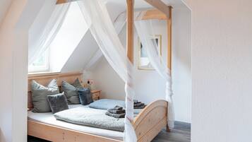 Un dormitorio con una cama de madera con dosel, una mesita de noche y un ventanal con cortinas translúcidas.