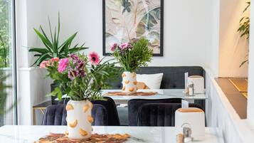 Uma sala de jantar moderna com mesa de vidro, cadeiras pretas e dois vasos com plantas.