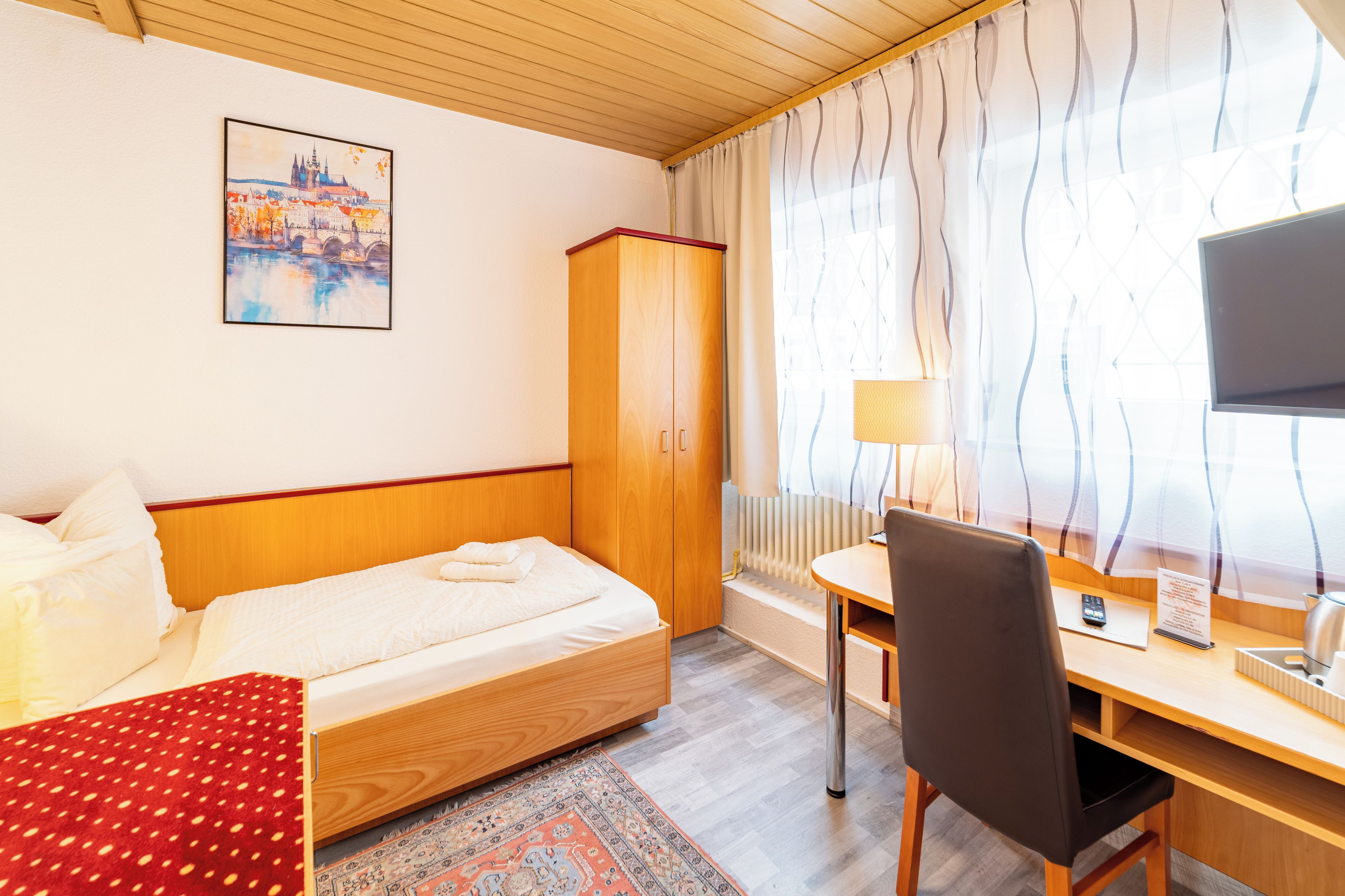Een hotelkamer met een bed, een bureau met stoel, een televisie, een kledingkast en een schilderij aan de muur.