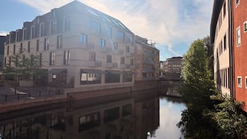 Un edificio moderno con una masa de agua reflectante al frente, un puente y arquitectura tradicional adyacente.