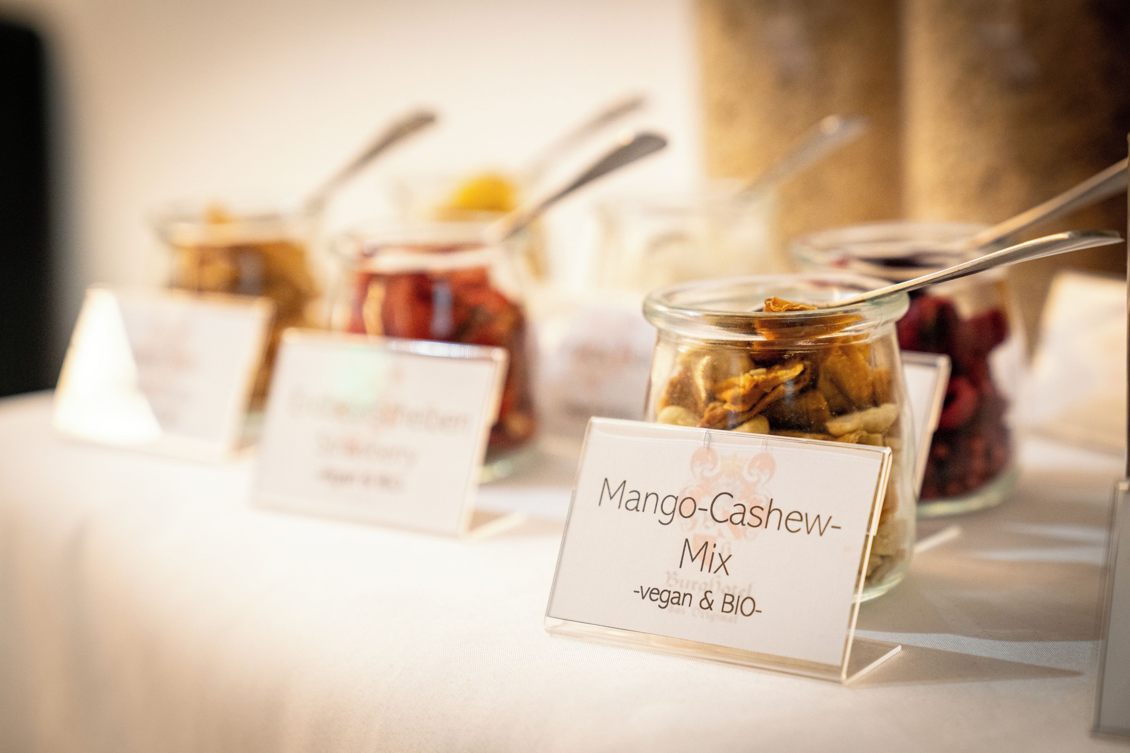 Una mesa de buffet con recipientes de comida etiquetados, incluyendo una mezcla de mango y anacardo.