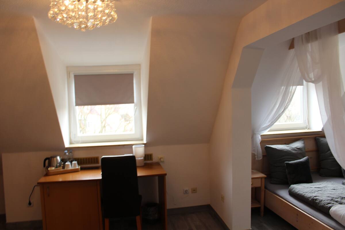 A small, cozy room with a desk, chair, and a bed with a canopy.