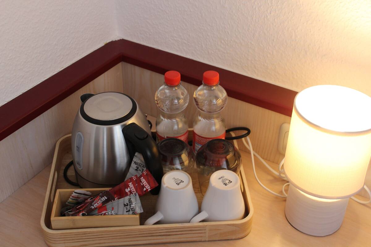A wooden tray with a kettle, two bottles of water, a coffee maker, a cup, and a lamp.