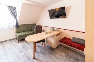 Una habitación moderna y funcional con un escritorio de madera, un sofá verde, un banco rojo con lunares y un televisor montado.