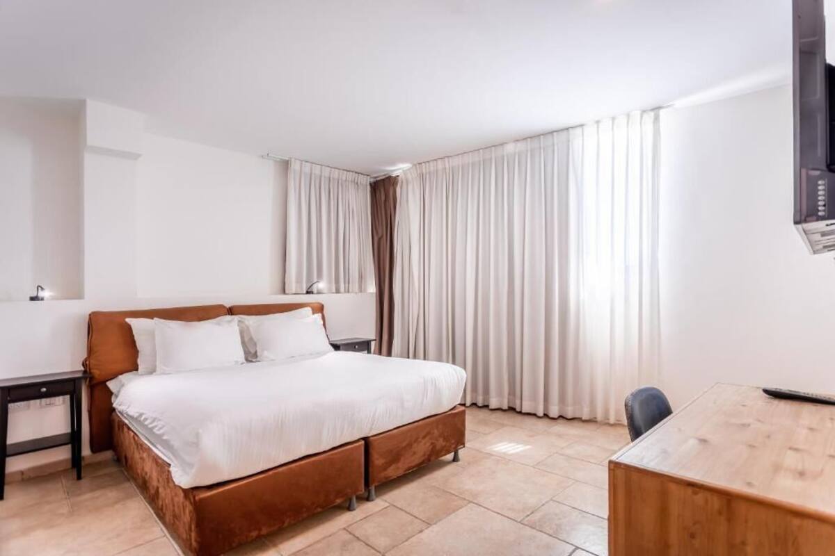 Quarto de hotel com cama, escrivaninha, cadeira, televisão e cortinas.