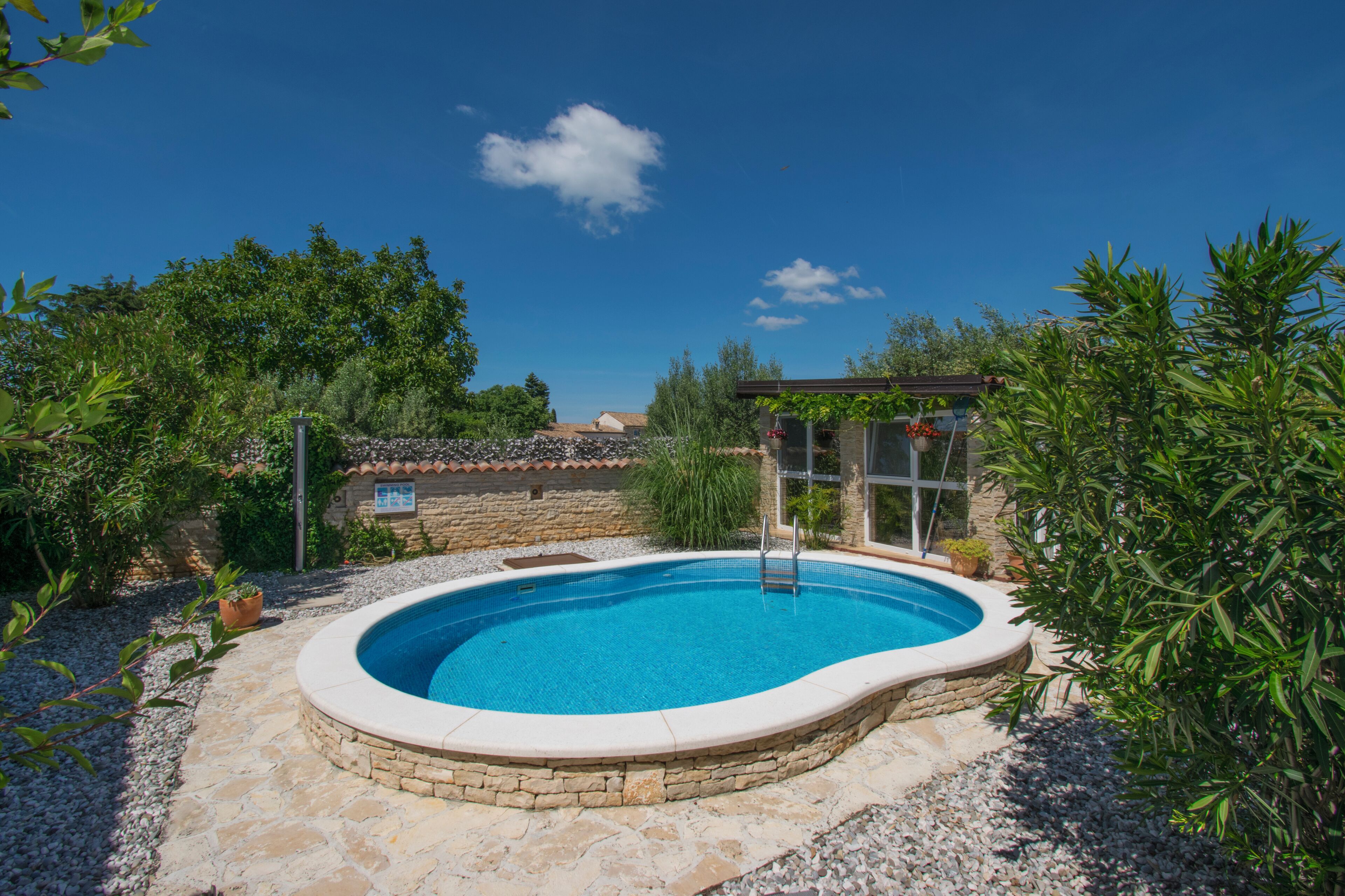 Une piscine entourée de murs de pierre et de verdure, sous un ciel bleu azur.