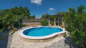 Ein Schwimmbecken, umgeben von Steinmauern und Grünpflanzen, mit blauem Himmel darüber.