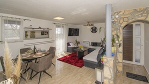Ein modernes Wohnzimmer mit Kamin aus Stein, einem Essbereich mit rotem Teppich und einer gemütlichen Sitzecke mit Sofa und Sesseln.