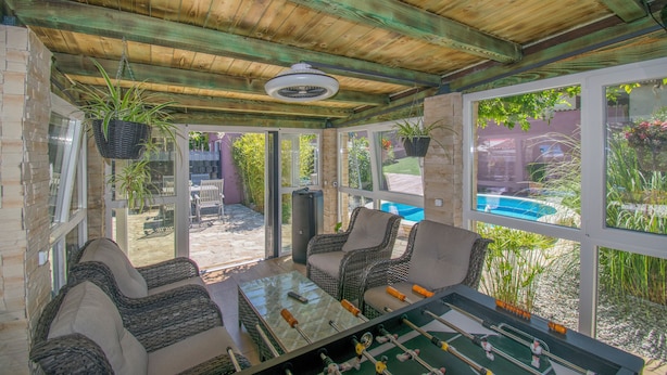 Ein überdachter Patio-Bereich mit Korbmöbeln, einem Tischkicker und Topfpflanzen.