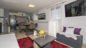 Ein modernes Wohnzimmer mit grauem Sofa, Teppich in Rot und Weiß sowie einem Essbereich mit Tisch und Stühlen.